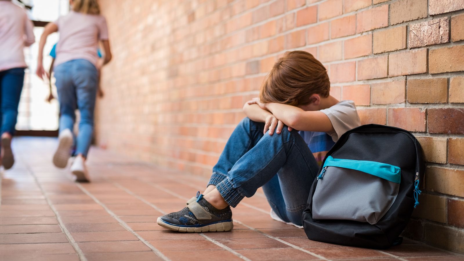 Depressives Kind sitzt in der Schule an einer Mauer