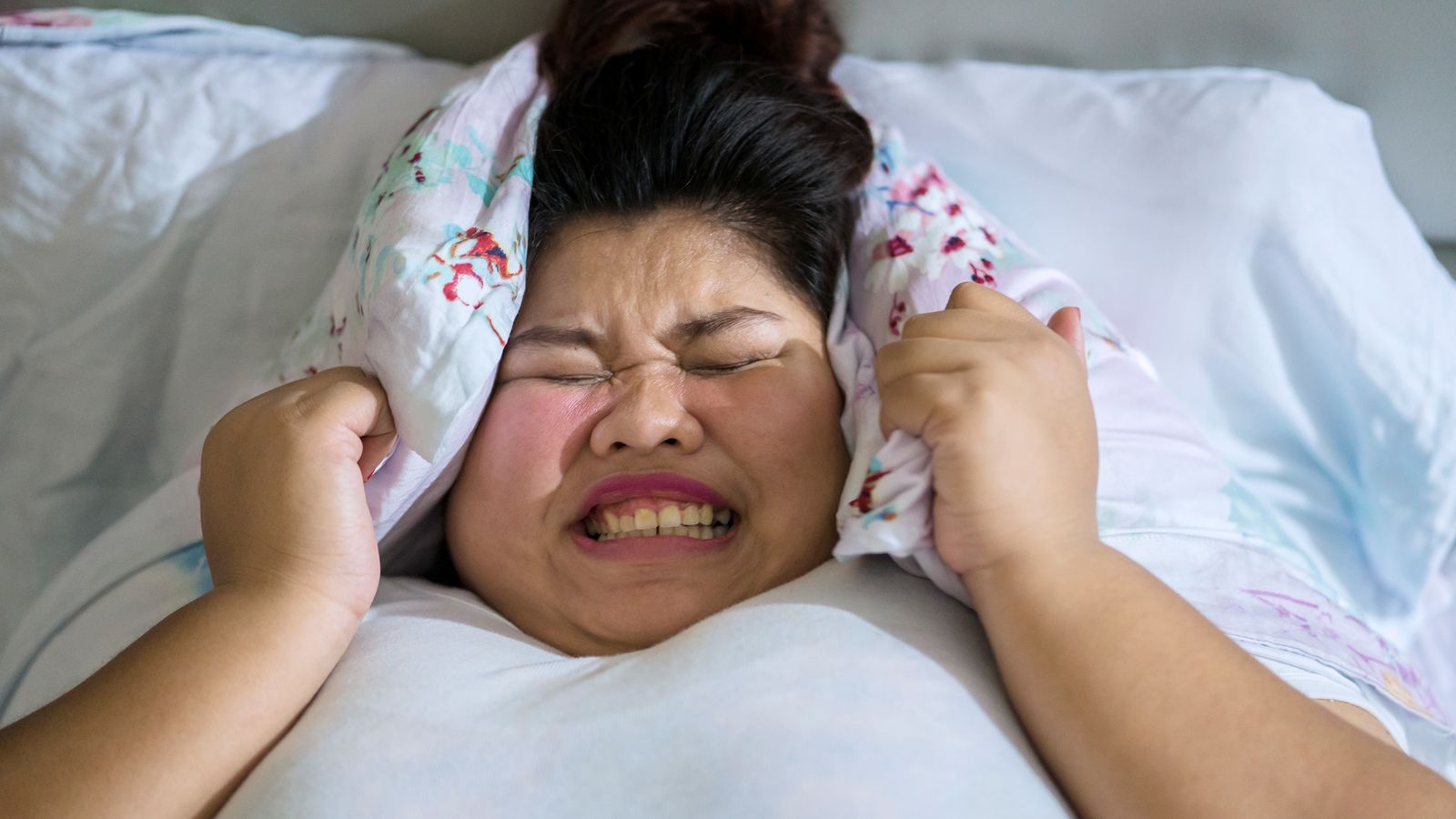 Übergewichtige Frau liegt mit starken Migräne-Schmerzen im Bett
