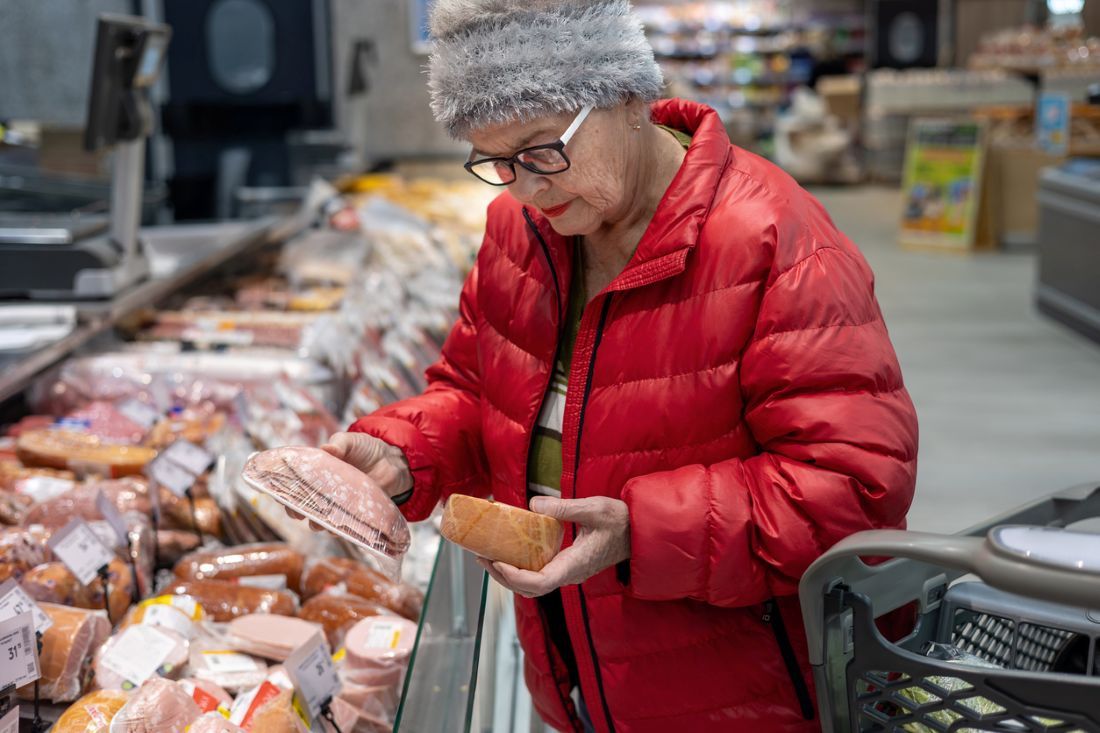 Ältere Frau vergleicht Wurstpreise in der Fleischabteilung des Supermarkts
