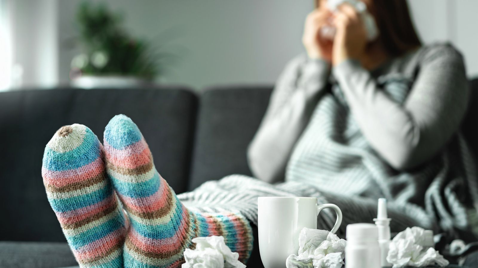Eine junge Frau liegt mit einer Erkältung auf dem Sofa