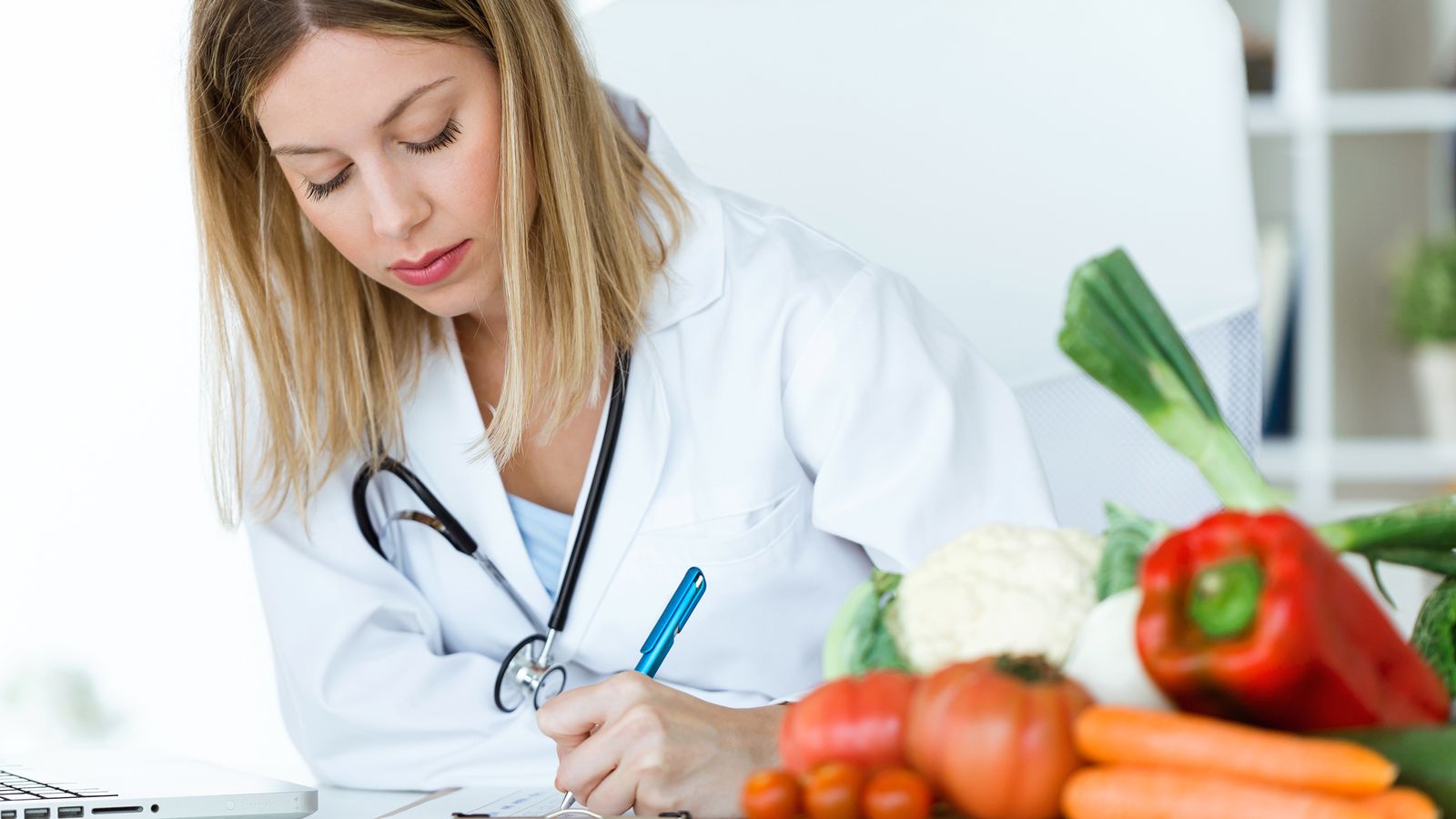 Ärztin füllt ein Formular über gesunde Ernährung aus. Im Vordergrund: Gemüse