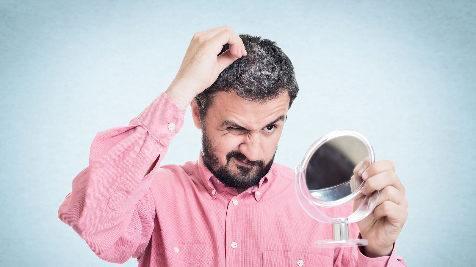 Mann betrachtet seine grauen Haare im Spiegel