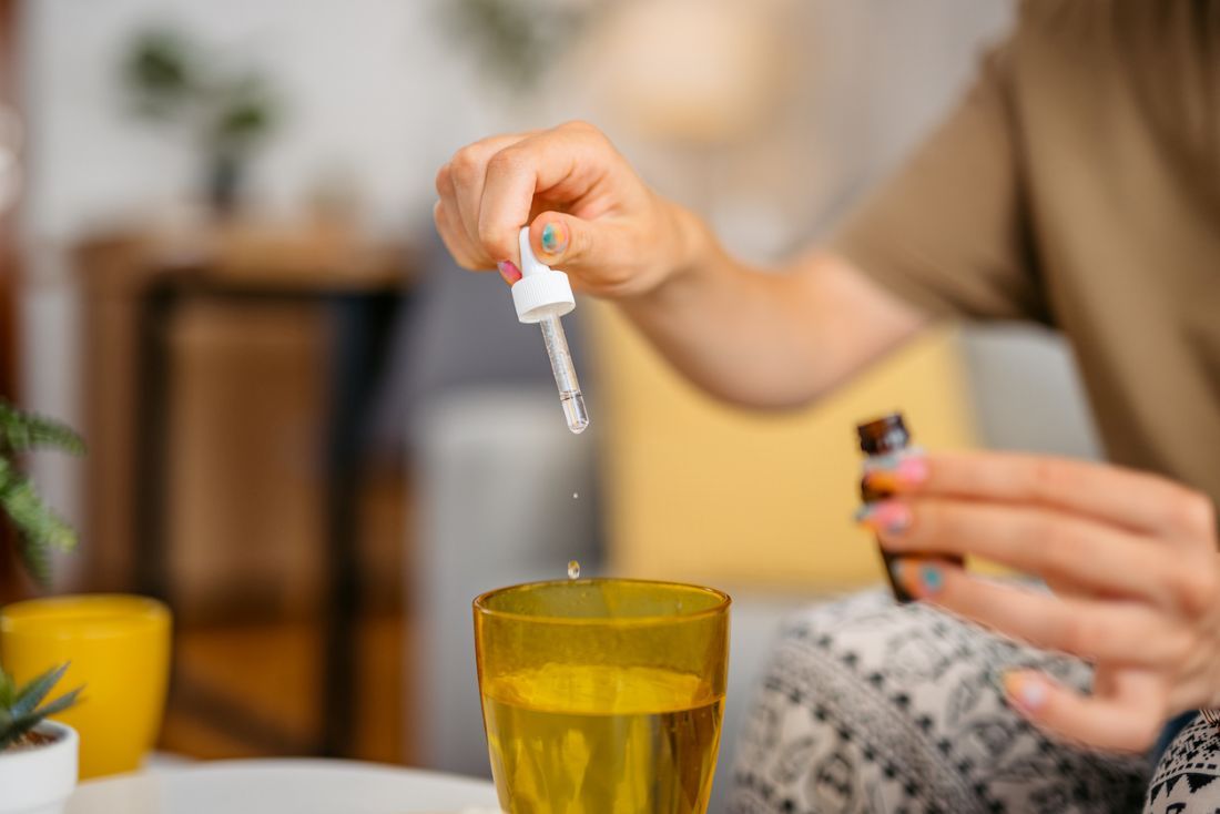 Junge Frau tropft Schwedenkräuter in ein Glas Wasser
