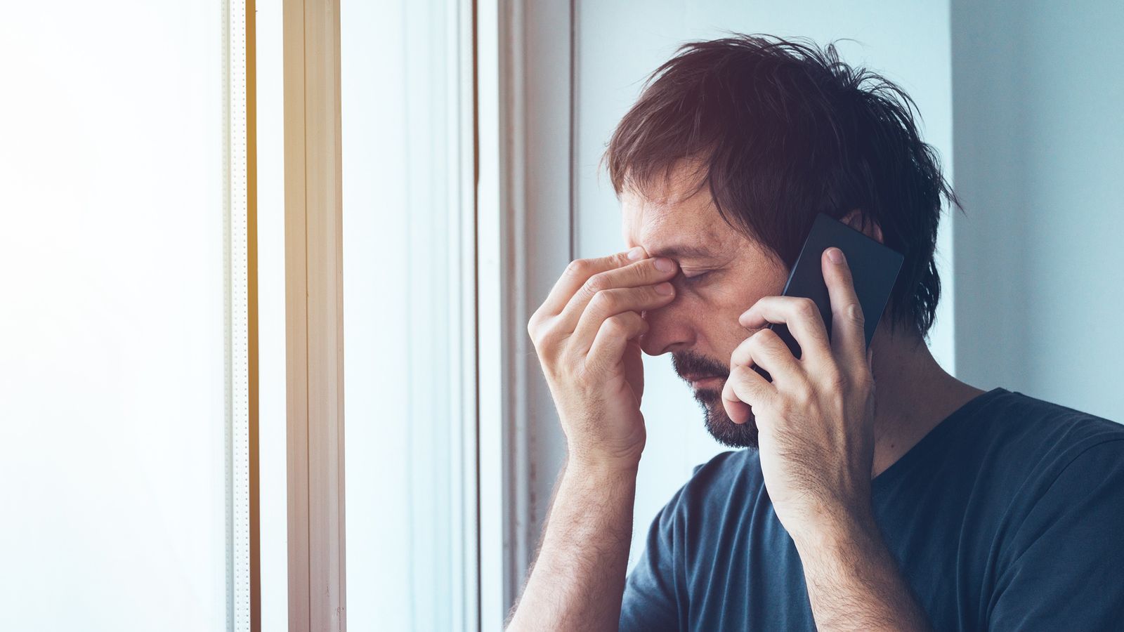Mann mit Kopfschmerzen telefoniert mit einem Mobiltelefon