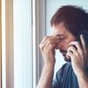 Mann mit Kopfschmerzen telefoniert mit einem Mobiltelefon