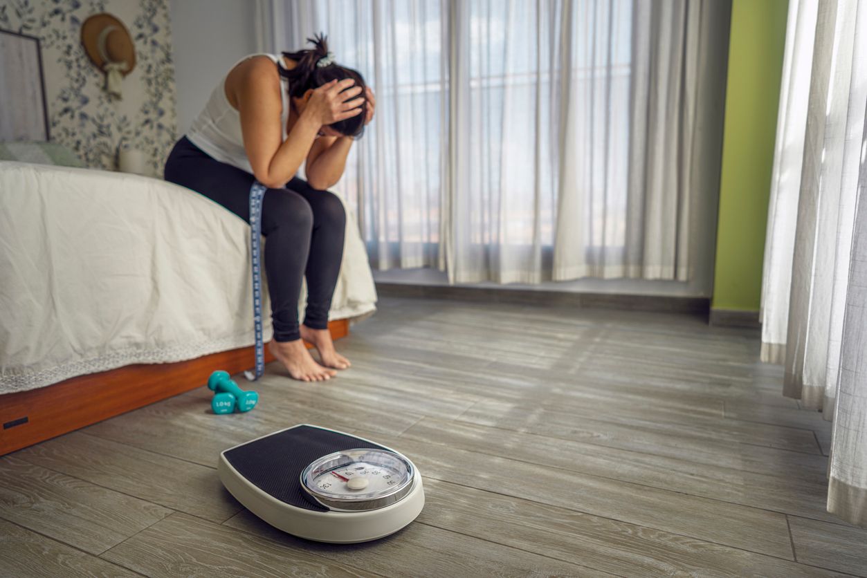 Frau blickt skeptisch auf eine Badezimmerwaage und hinterfragt den Body-Mass-Index