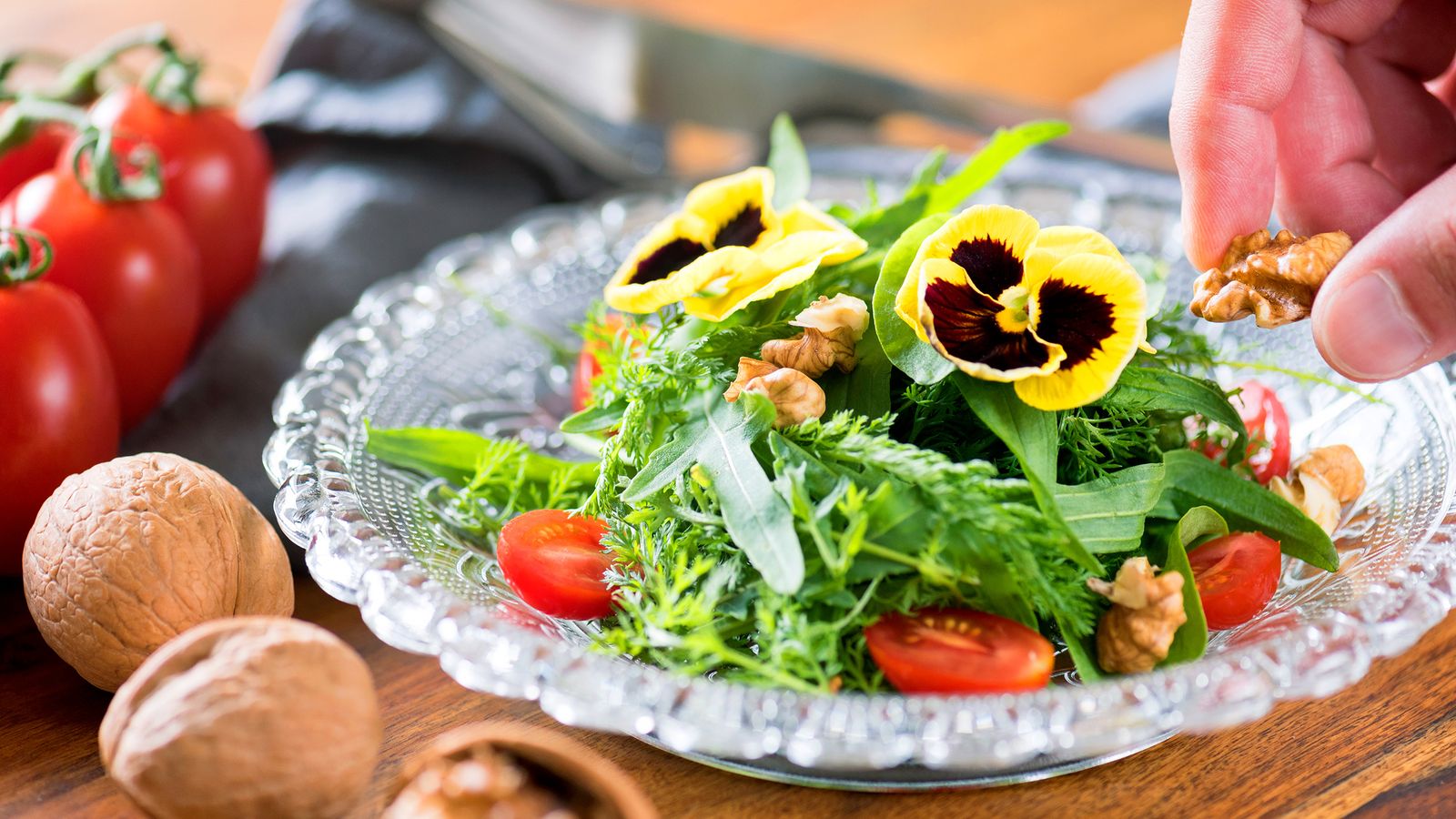 Gemischter Salat mit Walnüssen und Blumen garniert in einer Glasschüssel