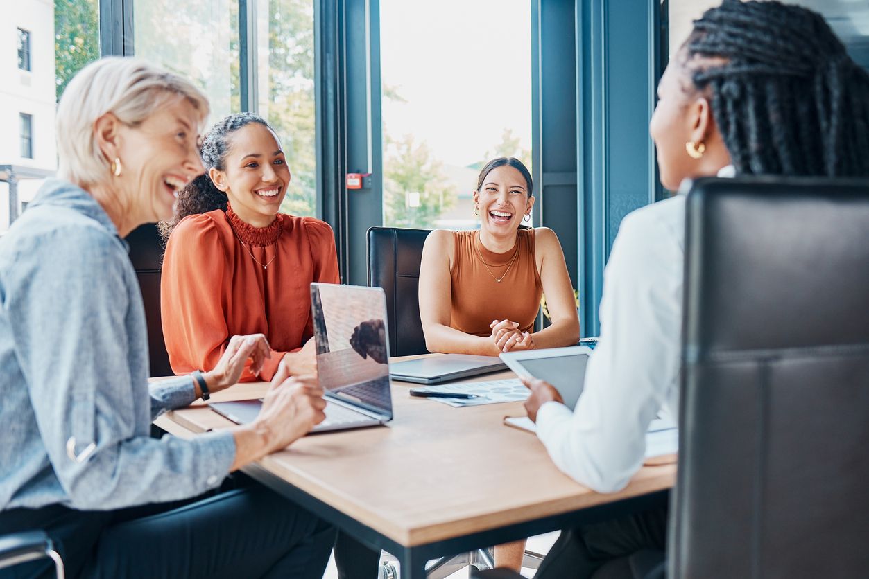 Vier Frauen sitzen an einem Konferenztisch und lachen