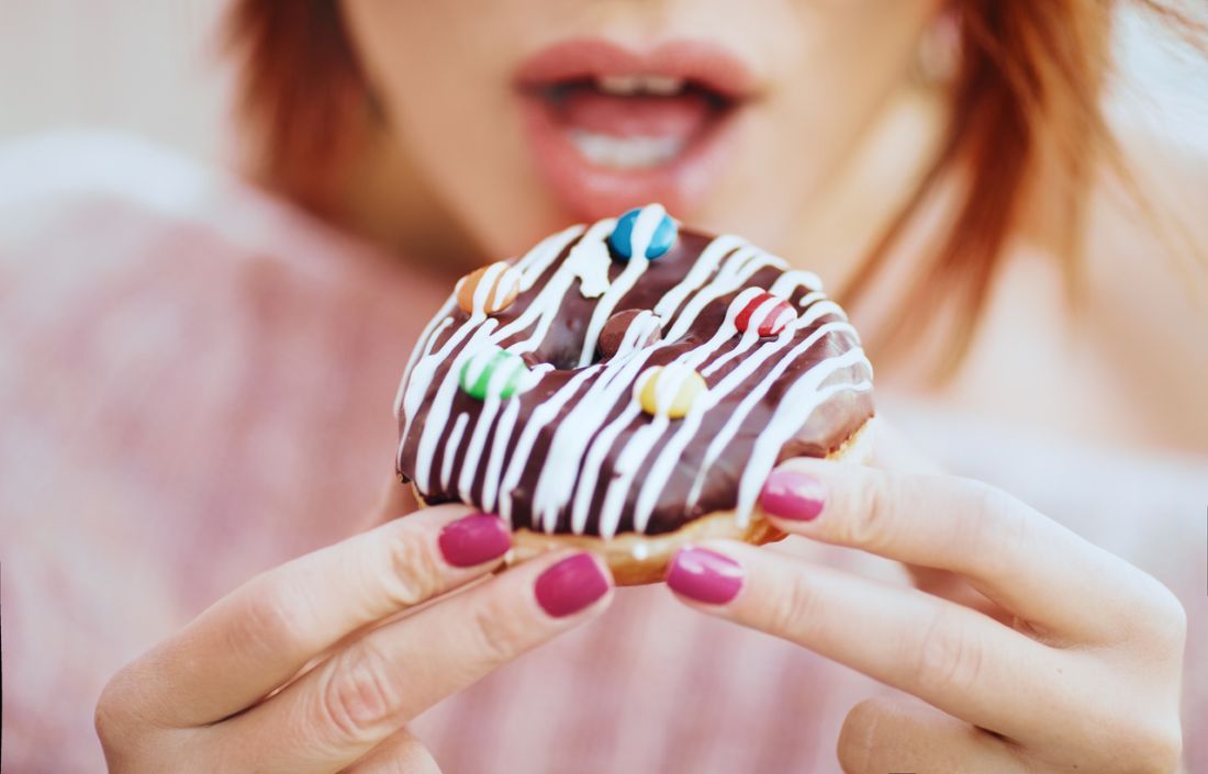 Unerkennbare junge Frau isst leckeren Donut.
