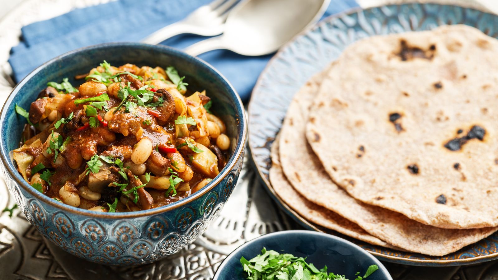 Bohnen Curry mit Chapatis in blauen Schüsseln und Tellern serviert