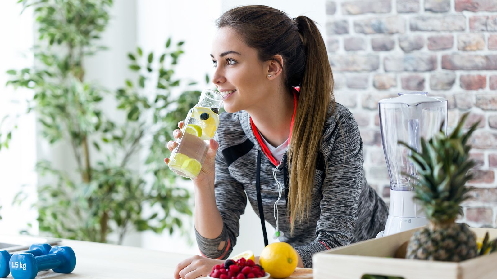 Junge, sportliche Frau trinkt Wasser mit Zitronenscheiben