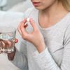 Frau hält ein Glas Wasser und eine Medikamentenpille in der Han