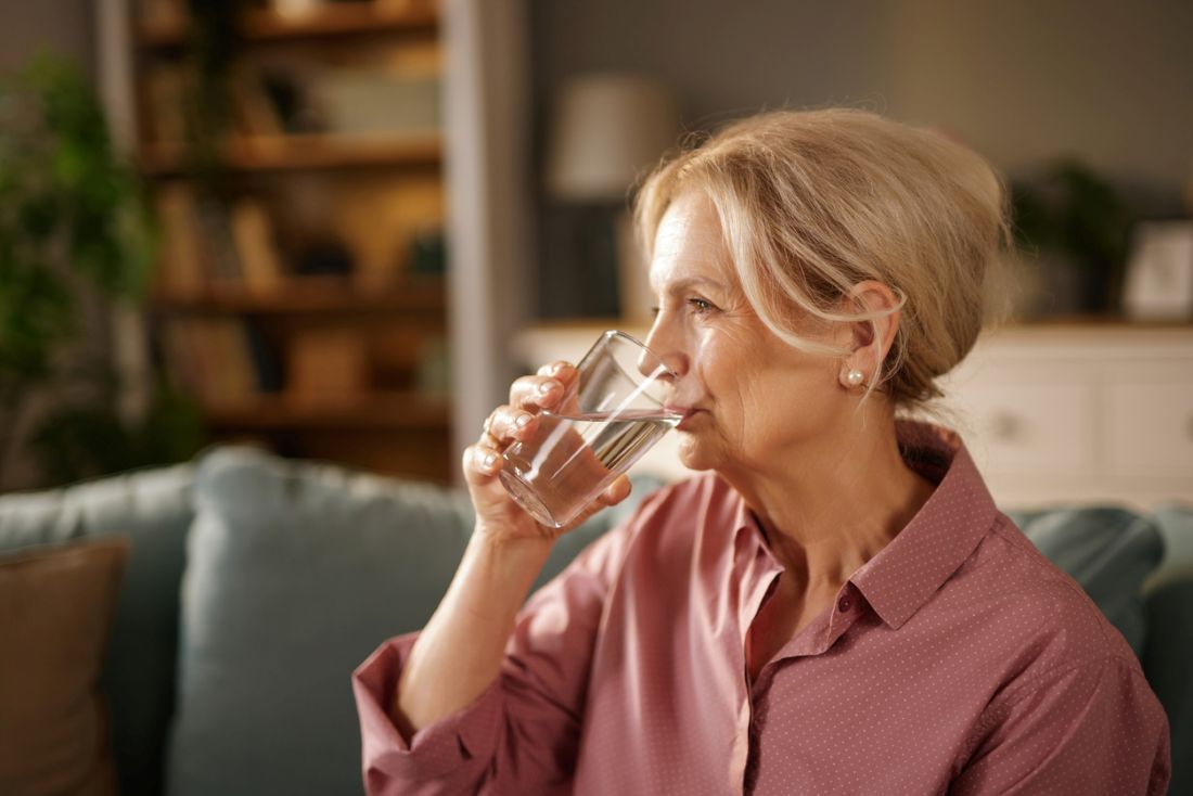 Seniorin trinkt Wasser auf dem Sofa zu Hause