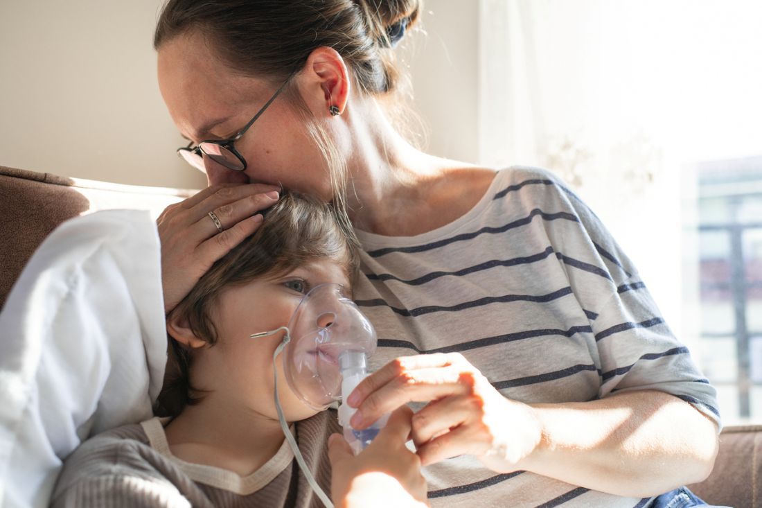 Krankes Kind mit Mutter inhaliert mit Vernebler zu Hause im Bett mit einer Lungenentzündung