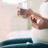 Hochschwangere Frau nimmt Medikamente mit einem Glas Wasser