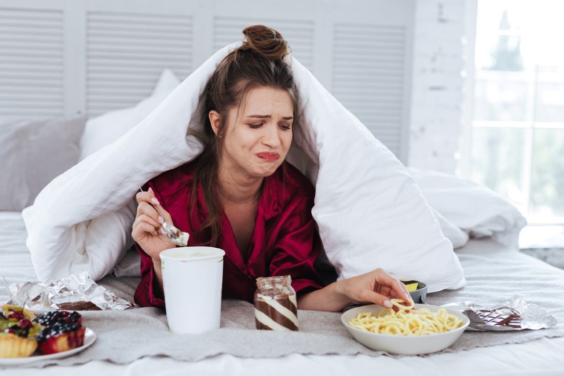 Weinende Frau liegt in ihrem Bett umgeben von snacks