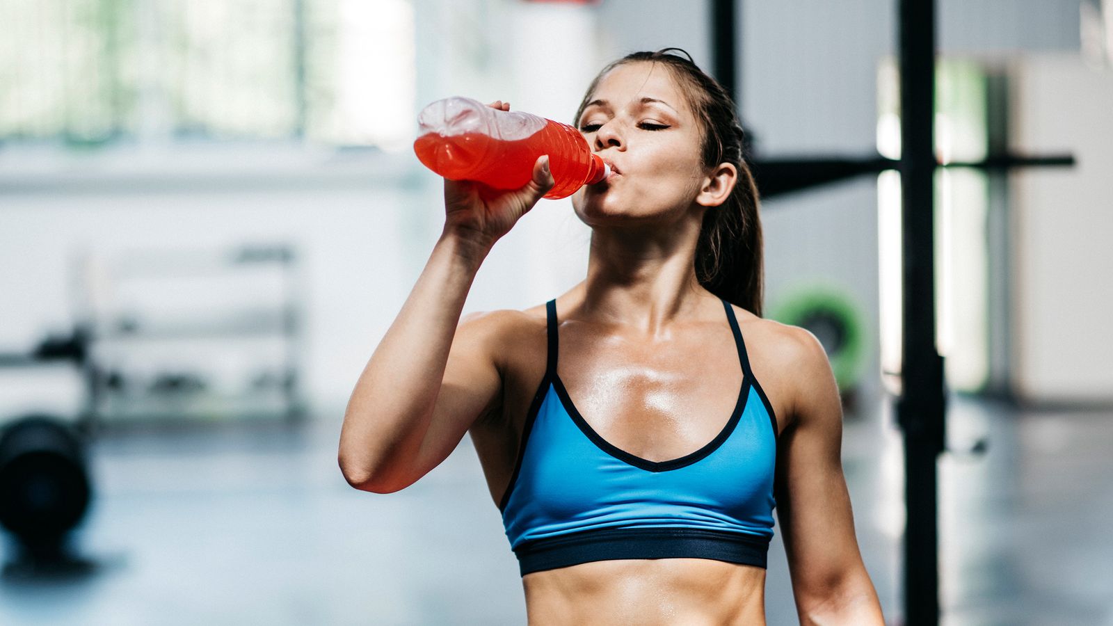 Junge sportliche Frau trinkt nach dem Training im Fitnessstudio einen Softdrink aus einer Plastikflasche
