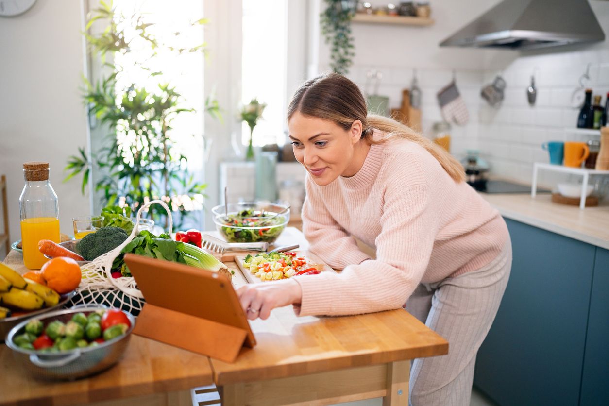 Schwangere Frau macht Salat, während sie dem Online-Rezept auf einem digitalen Tablet folgt
