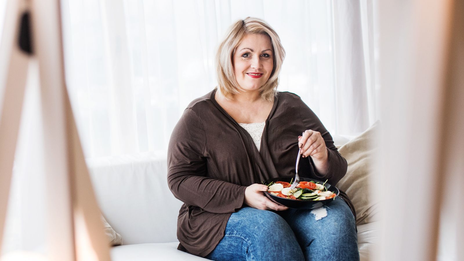 Übergewichtige Frau sitzt auf einem Sofa und isst einen Salat