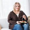 Übergewichtige Frau sitzt auf einem Sofa und isst einen Salat