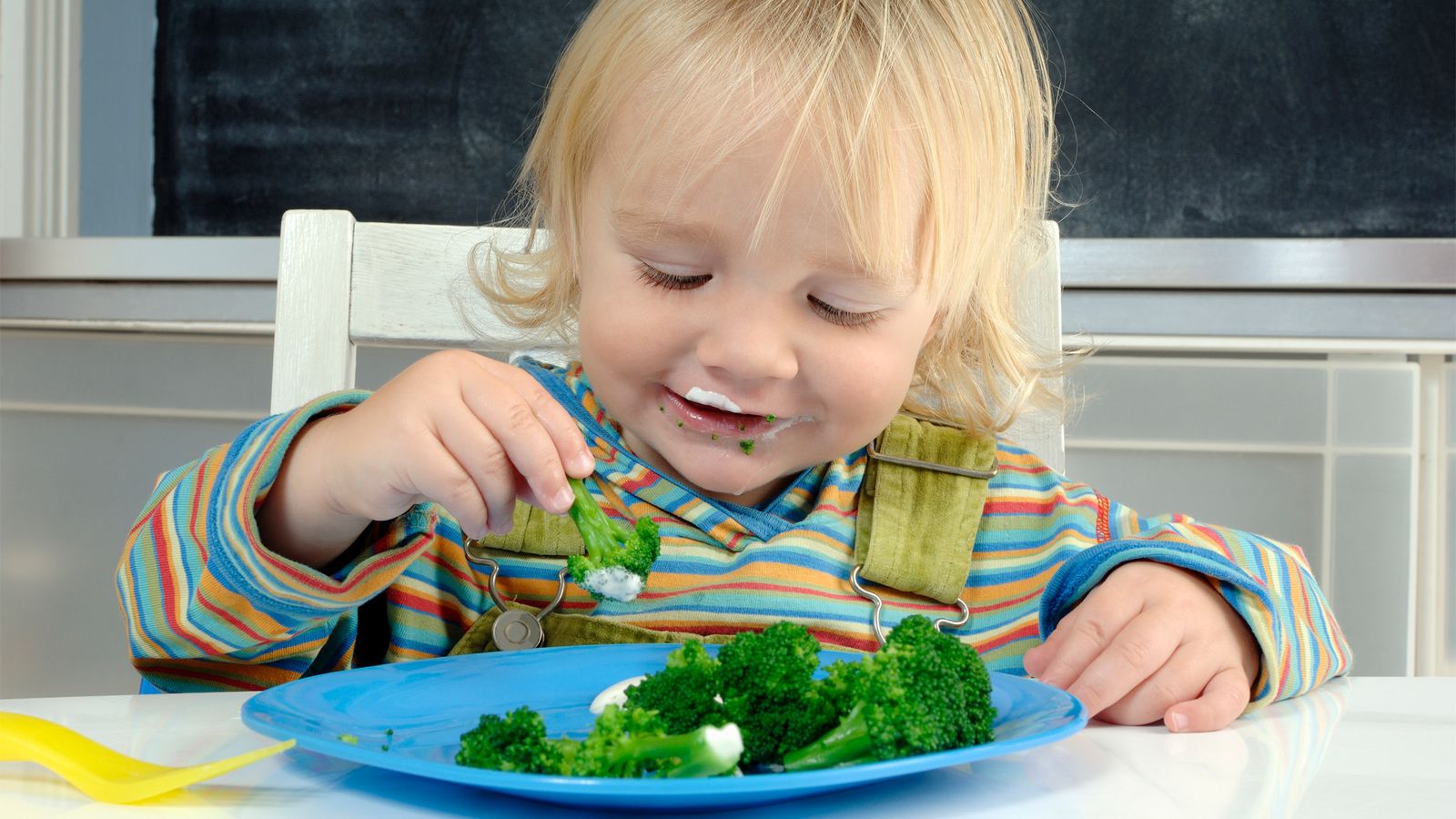 Kind isst Brokkoli aus einem blauen Teller