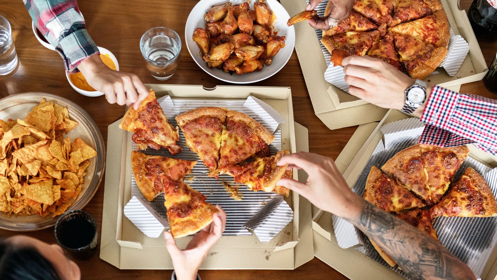 Fastfood: Pizza, Chicken Wings und Tortilla-Chips auf einem Tisch