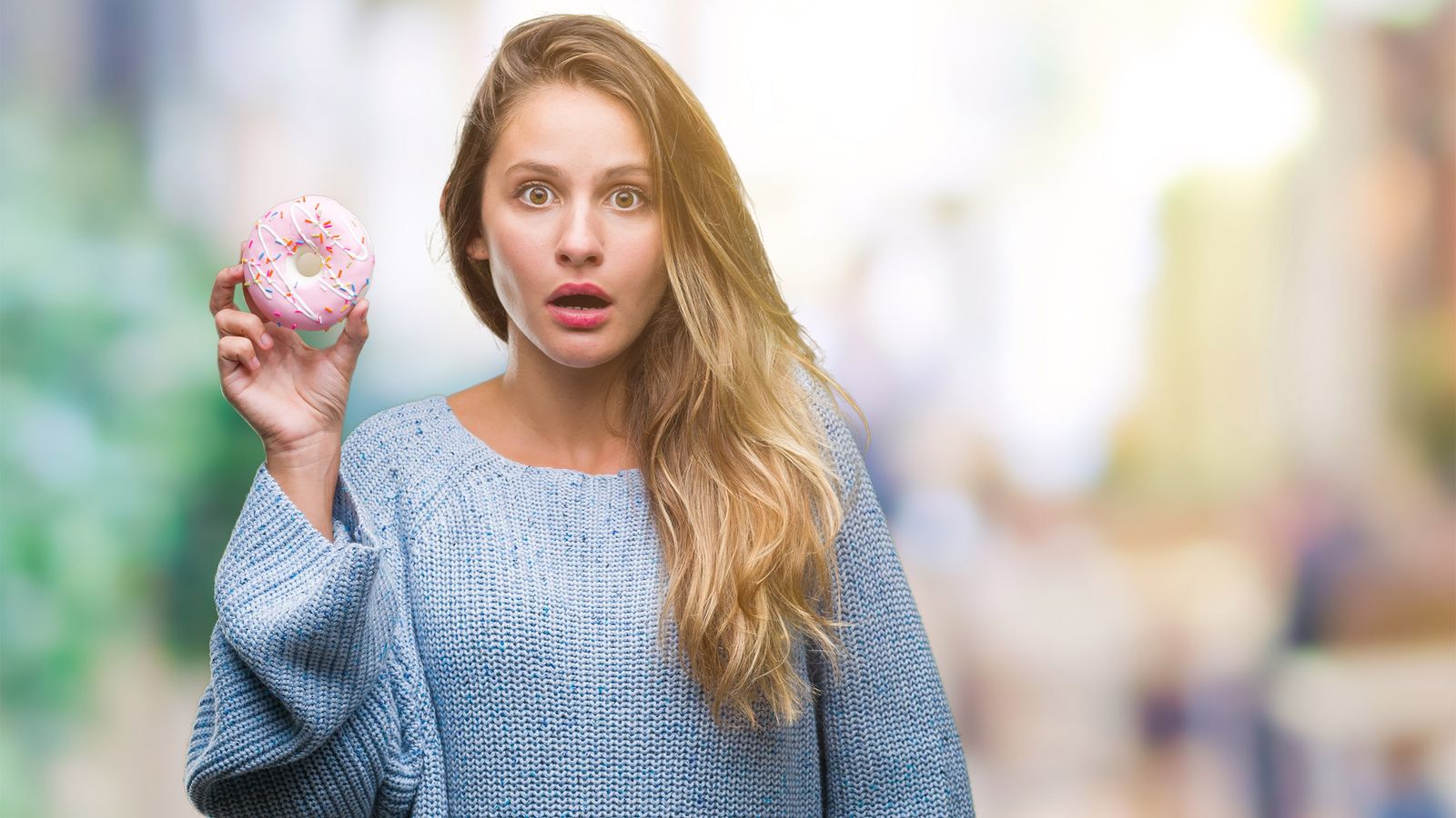 Frau hat einen Donut in der Hand und ist geschockt, dass Zucker Herzkrankheiten fördert