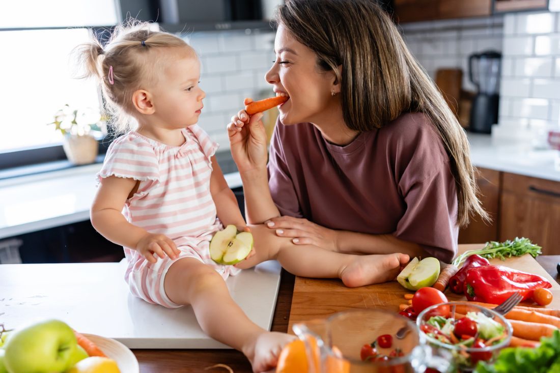 Fröhliche Mutter und ihr süßes kleines Baby essen gesundes Obst und Gemüse