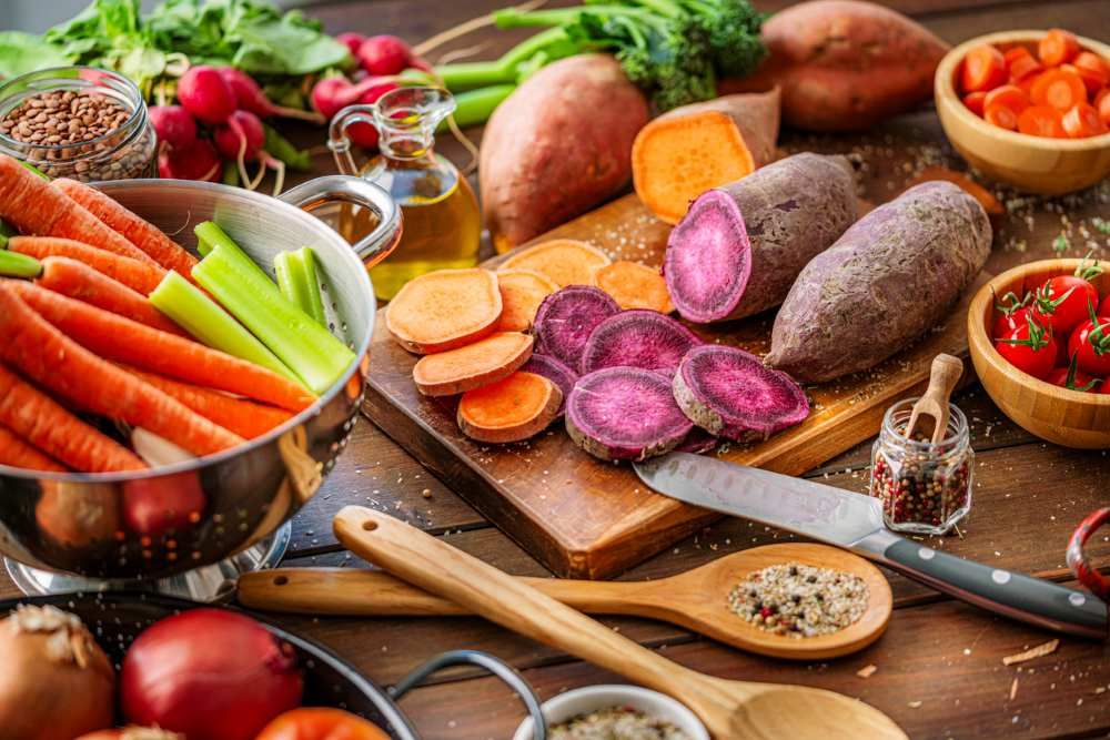 Ganz und in Scheiben geschnittene, rohe lila und gelbe Süßkartoffeln auf dem Schneidebrett. Kochen gesunder und frisch gepflückter Wurzelgemüse