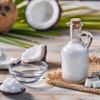 Glasflasche mit Kokosöl und frische Kokosfrüchte auf rustikalem weißem Holzhintergrund