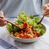 Junge Frau mischt Zutaten in ihrem gesunden, frischen veganen Salat