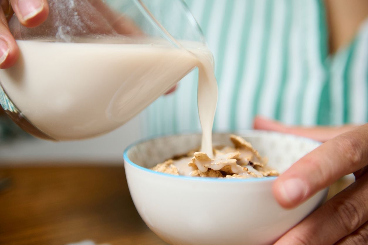 Milch in eine Schüssel mit gesundem Vollkorngetreide gieße