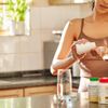  Aufnahme einer unkenntlichen Frau, die allein in ihrer Küche steht und ihre Vitamine nimmt 