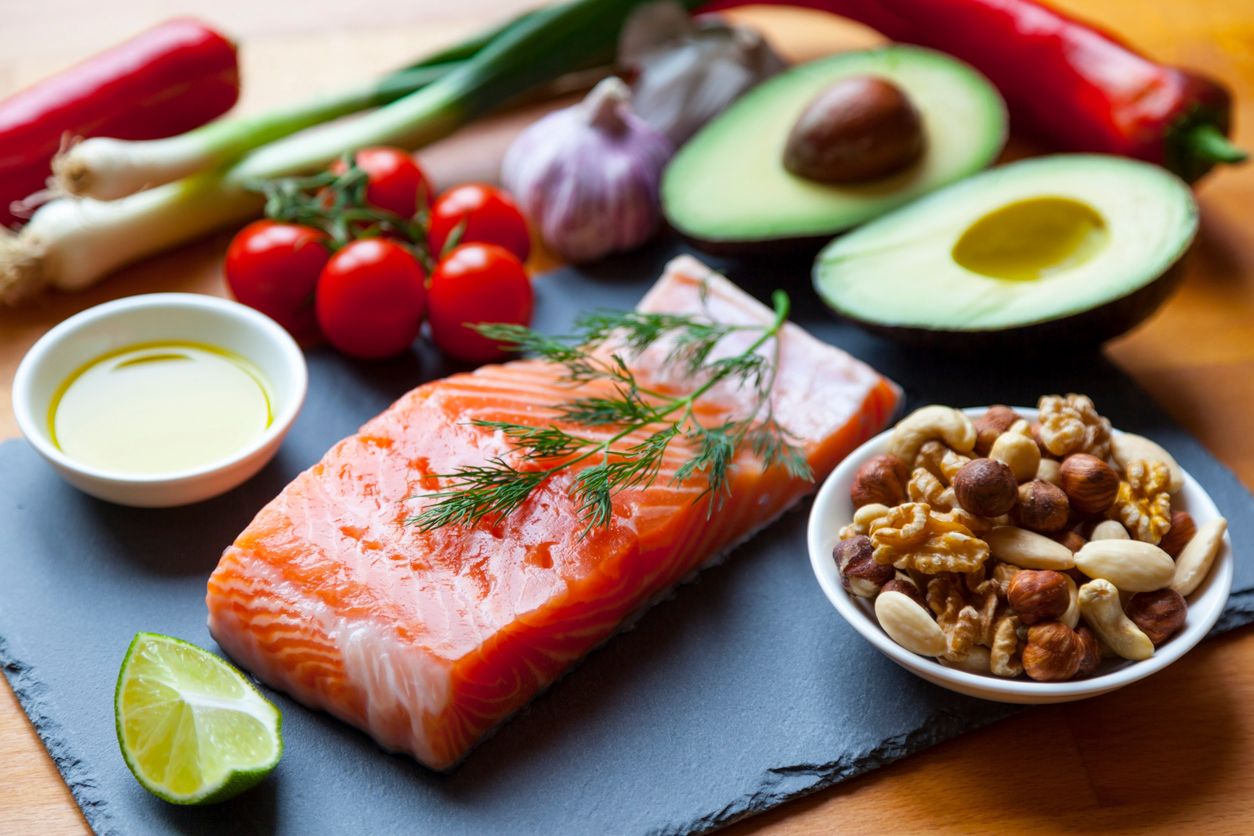 Lebensmitteln mit hohem Gehalt an gesunden Fetten wie Lachs, Olivenöl, Nüssen und Avocados mit Gemüse und Kräutern