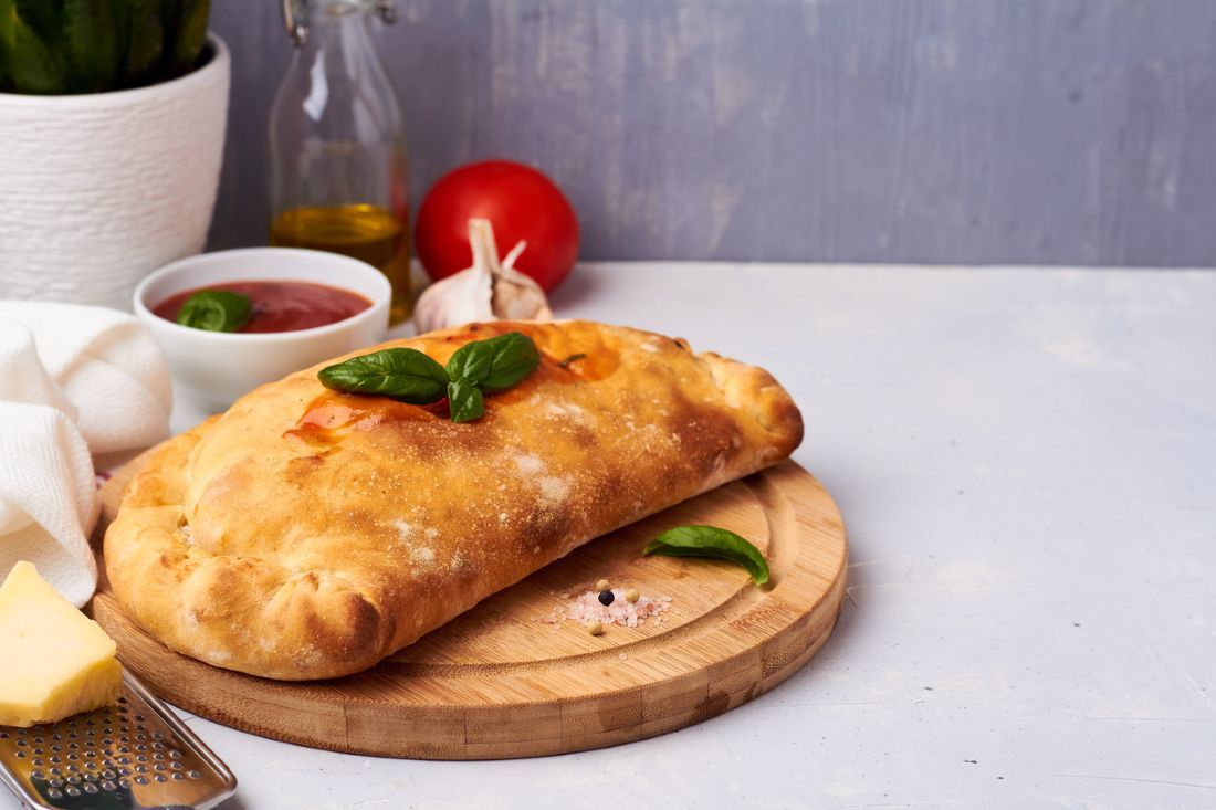 Pizza Calzone – Gefüllt mit Paprika, Mais und Champignons auf einem Brett