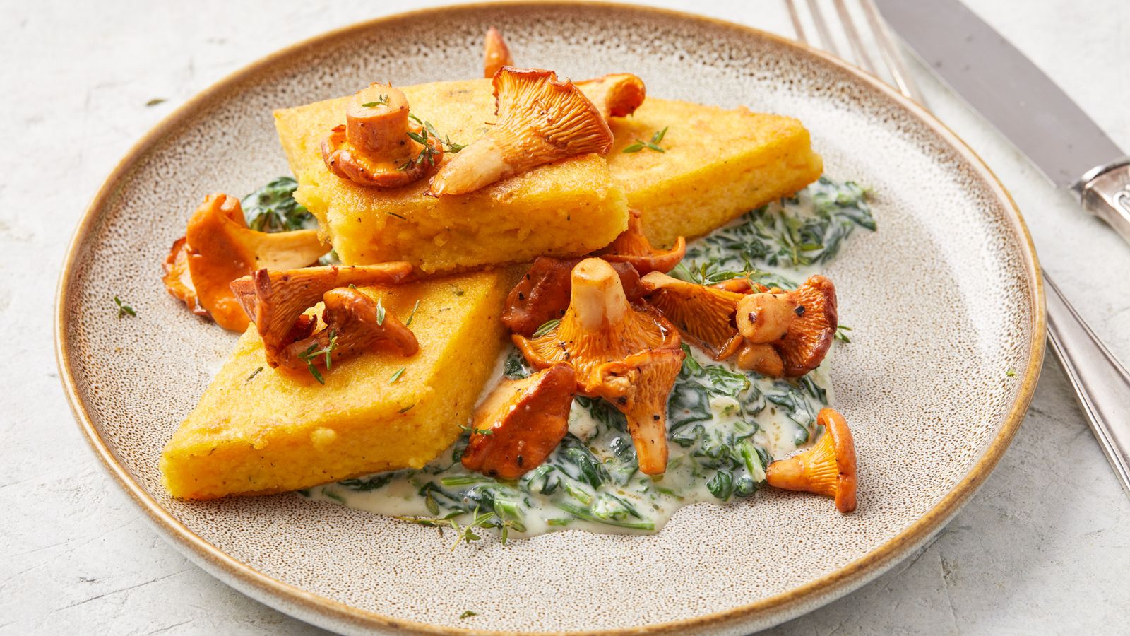 Polenta-Schnitten mit cremigem Spinat und gebratenen Pfifferlingen auf einem Teller serviert