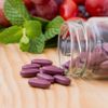 Resveratrol-Tabletten in einem Glas und farbige Früchte im Hintergrund