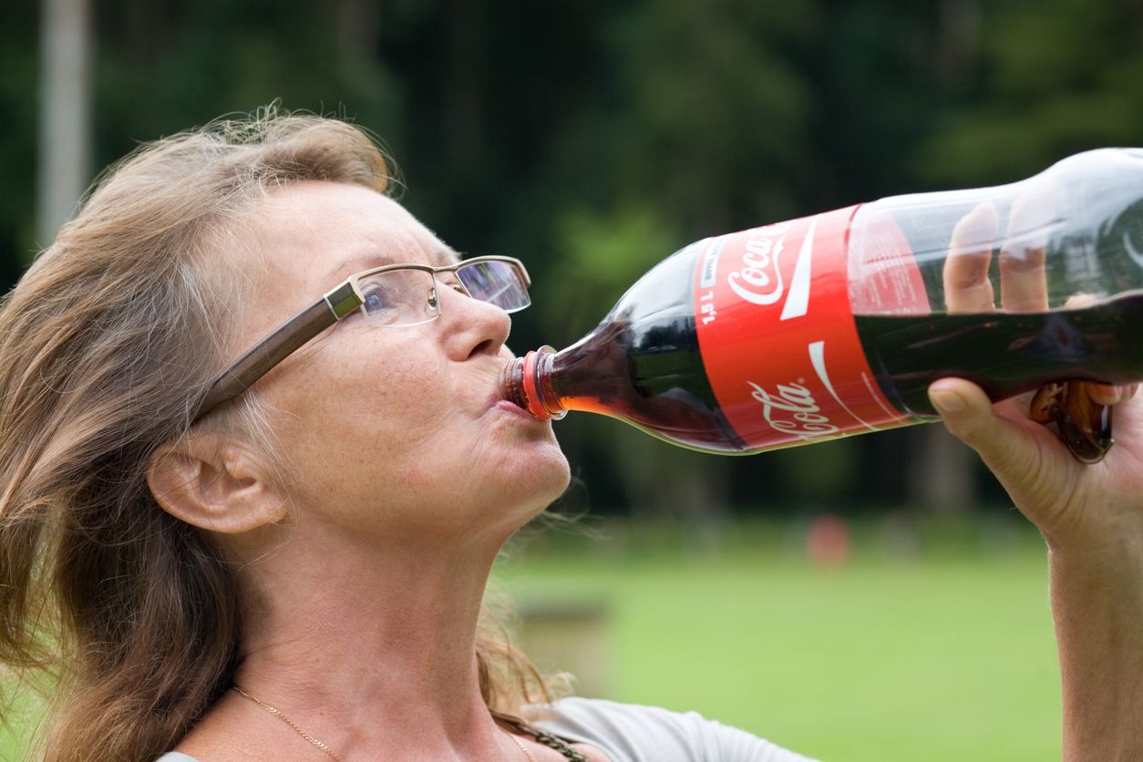 Ältere Frau trink aus einer Cola-Flasche