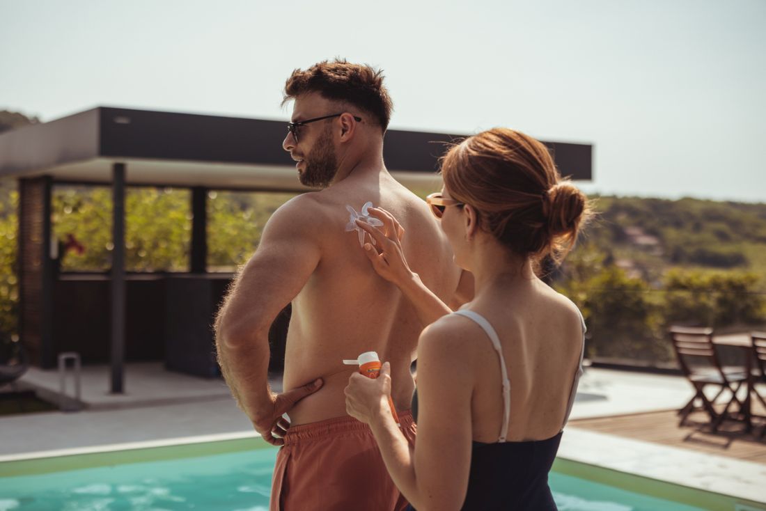 Frau, die Sonnencreme auf den Rücken des Mannes am Pool aufträgt