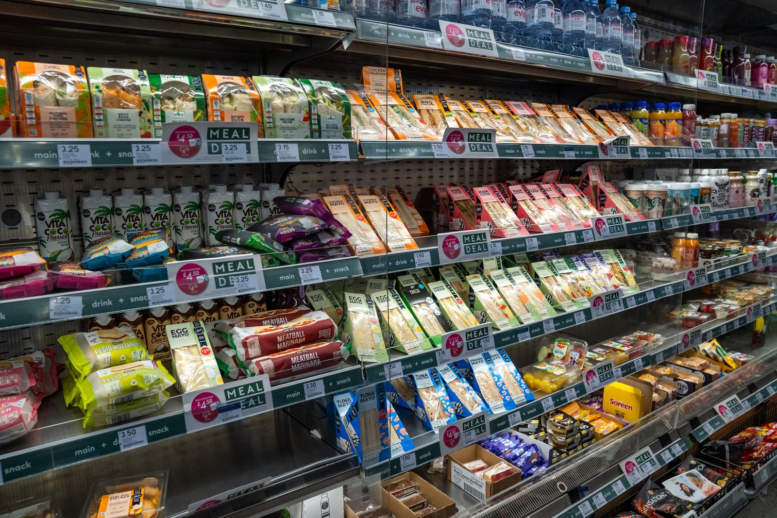 In einem Supermarktregal werden abgepackte Sandwiches, Snacks und Getränke ausgestellt, die den Käufern schnelle Essensangebote bieten.