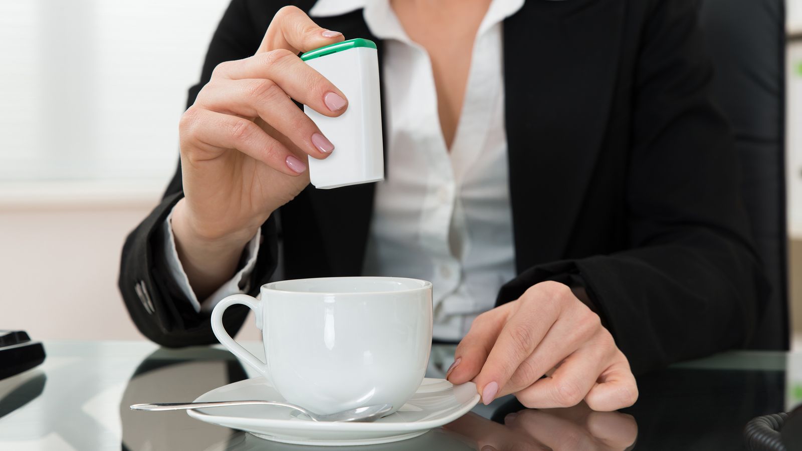 Frau lässt einen Süssstoff in den Kaffee fallen