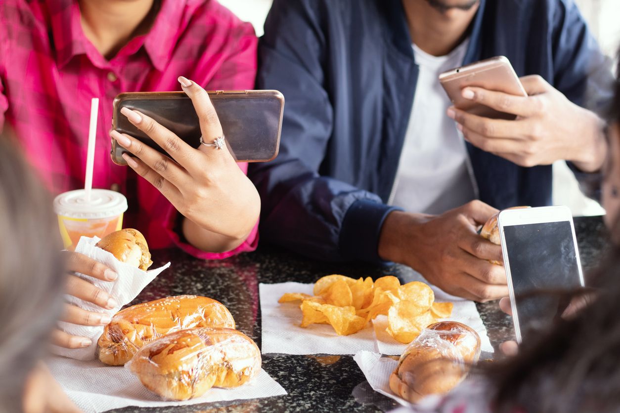 Gruppe von nicht wiederzuerkennenden Menschen beschäftigt auf dem Handy, während Snacks zusammen im Restaurant 