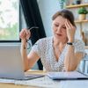 Gestresste Frau mittleren Alters, die zu Hause am Tisch mit Computer sitzt 