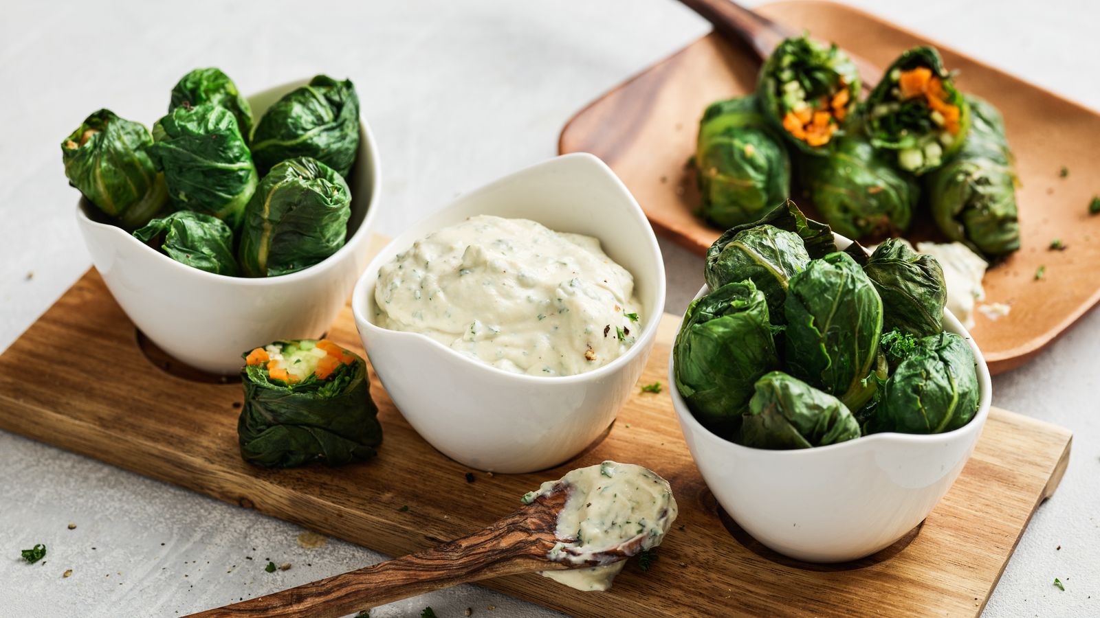 Lattich-Wraps mit Dip in weissen Schalen auf einem Holzbrett serviert