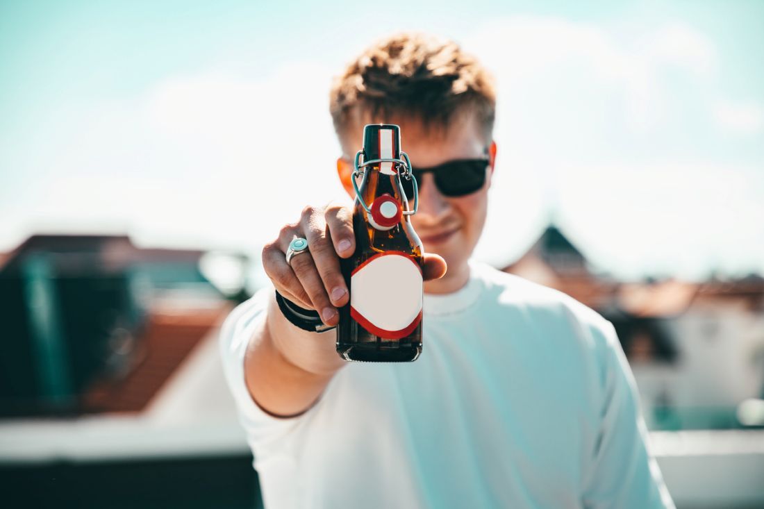 Junger Mann lädt zu einer Flasche Bier ein
