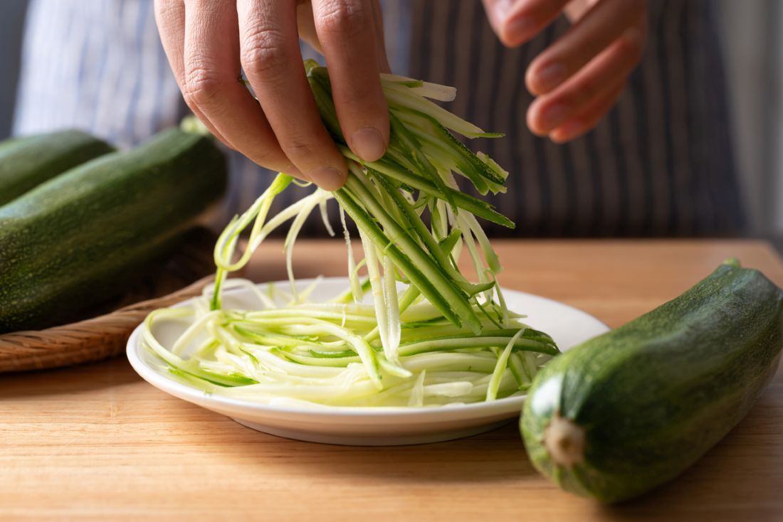  Frische Zucchini-Nudeln (Zoodles) auf einem weißen Teller mit den Händen